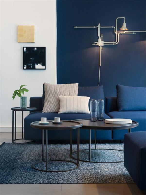 mėlyna sofa, mėlyna svetainės sienų spalva, juodi apvalūs stalai, šiuolaikiškas dekoras su dviem svetainės paveikslais