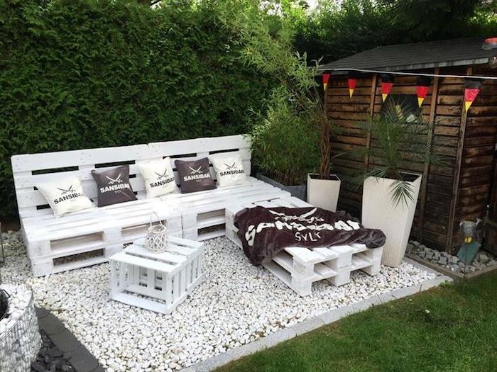 Beyaza boyanmış köşe kanepeli palet bahçe mobilyaları orijinal fikri, beyaz çakıl üzerinde palet sehpa, yeşil duvar