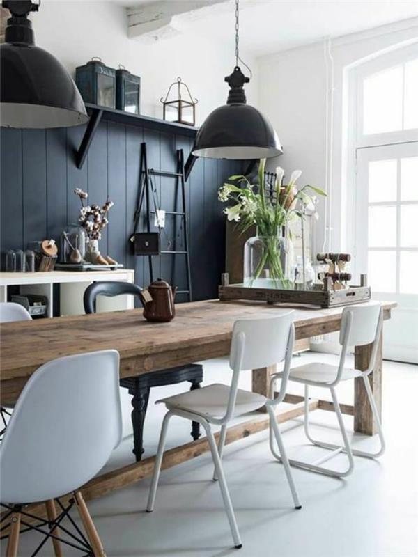 siena antracito pilka, pilki atspalviai perdažyti jo virtuvę, du dideli juodo metalo šviestuvai, baltos ir juodos kėdės, plastikas ir metalas, baltos grindys, didelis stačiakampis kaimiško stiliaus stalas