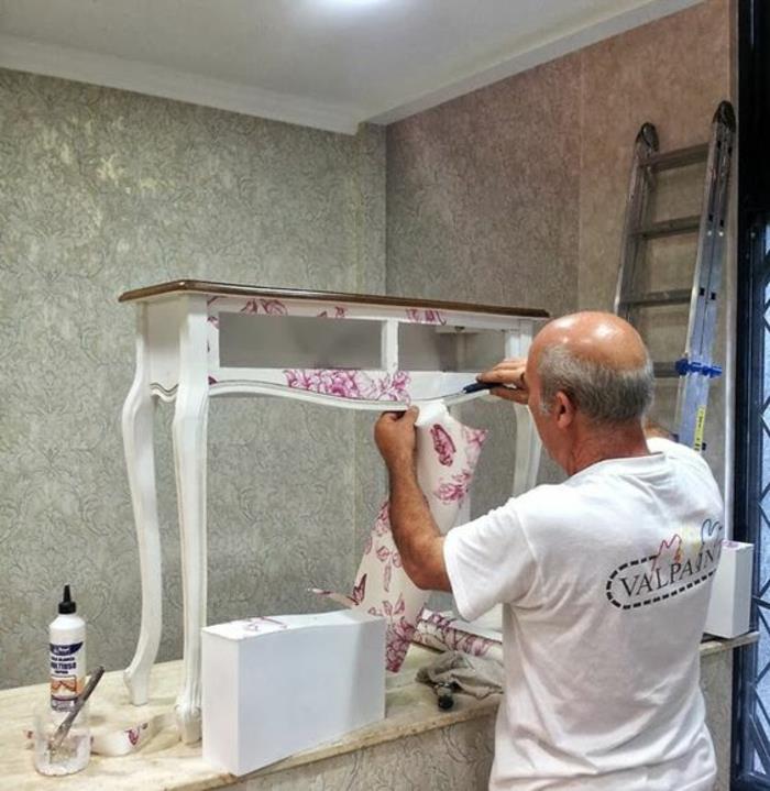 preobleka, lesena miza, pobarvana v belo in prekrito z belimi in rdečimi tapetami, omara z ukrivljenimi nogami, moški, ki dela na preobrazbi stare mize
