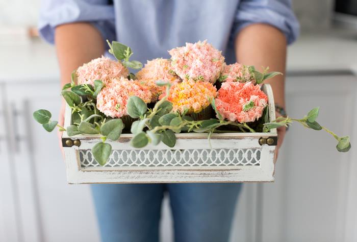 gana neįprasta gėlių kompozicija, pagaminta iš gėlių formos keksiukų senoviniame krepšelyje, mamos dienos veikla, skirta gurmanų dovanai
