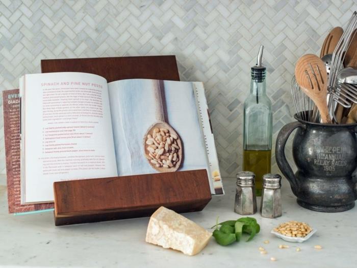 Tahtadan yapılmış yemek kitapları için stand, açık bir kitap, peynir parçası, fesleğen yaprağı ve fındık, çeşniler ve mutfak eşyaları yakınlarda