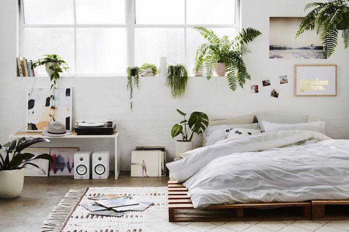 Paletna postelja v popolnoma beli nordijski deko spalnici z veliko zelenimi rastlinami in vinilnimi ploščami