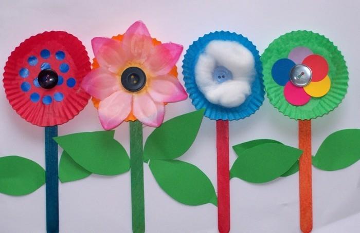 DIY projekti za otroke, štiri rože iz modelčkov za piškote v različnih barvah, pritrjene na sladoledne palčke, okrašene z listi zelenega papirja, gumbi in bombažem