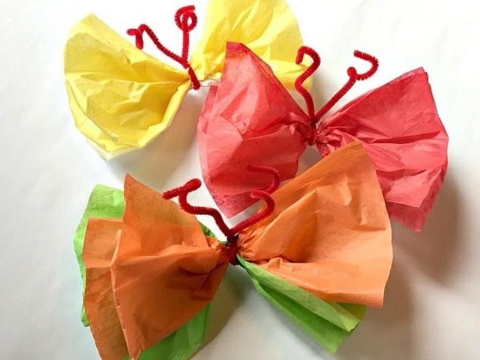 umetniški projekti diy, trije metulji iz krep papirja, v rumeni in rdeči, oranžni in zeleni barvi, vezani s preprosto rdečo mehko žico