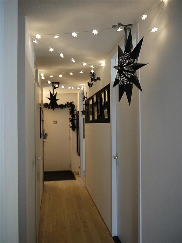 preprost ozek hodnik z belimi stenami in vrati, okrašen z osvetljenimi verižnimi lučmi v obliki zvezde, črnimi venci in velikimi črnimi zvezdnatimi lučmi