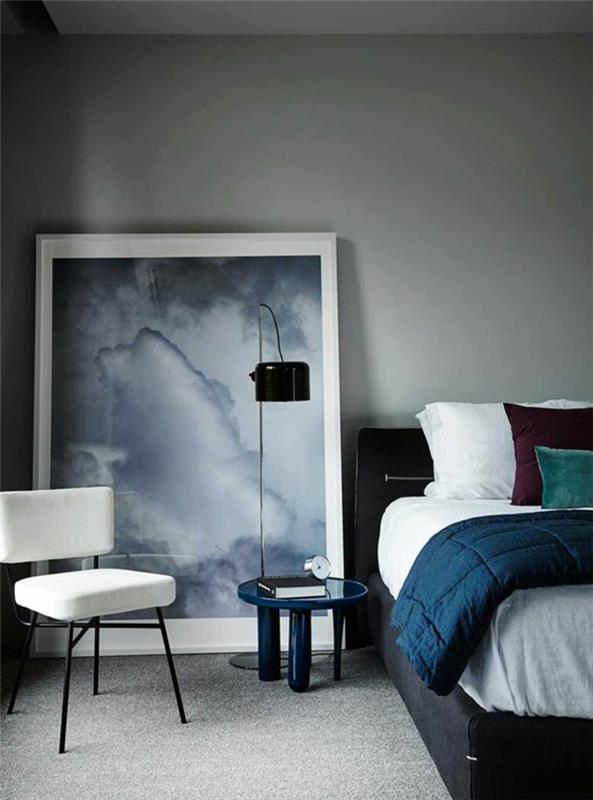 modra dekoracija spalnice za odrasle s svetlo sivo steno in veliko sliko s sivimi odtenki v belem okvirju
