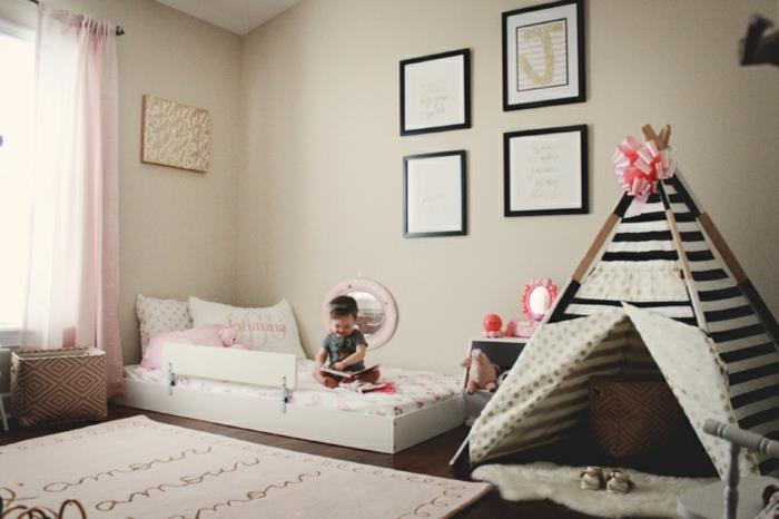 „Montessori“ miegamasis, lova ant grindų, vaiko titai, juodos ir baltos juostelės, rožinė juostelė, žaidimų kilimėlis, sienų apdaila, rudas laminato parketas