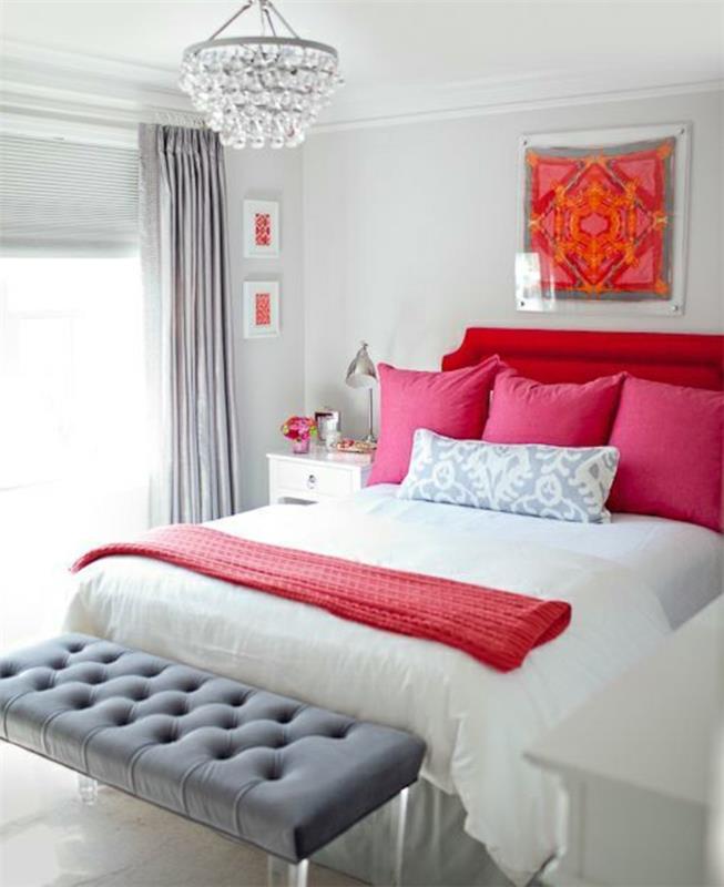 roza in siva spalnica, bela stena, siv konec postelje in zavese, eleganten lestenec, bela posteljna garnitura in roza blazine, rdeče vzglavje