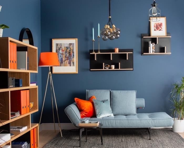 sodobna dekoracija doma s polnočno modro dnevno sobo z oranžnimi poudarki, blazino, oranžno svetilko, izvirno črno polico, stekleno visečo lučjo