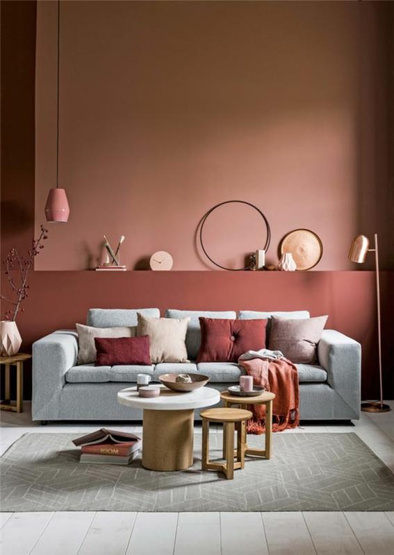 stena v barvi lososa, siv kavč, klubska mizica, leseni stolčki, roza viseča svetilka