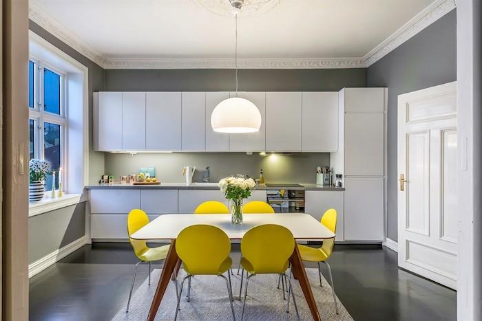 gri boya ile yeniden boyanmış duvar, gri mutfak dolabı, beyaz sarkıt lamba, gri zemin ve sarı sandalyeler ve beyaz masa ile yemek odasına açılıyor