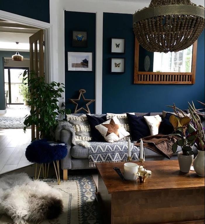 eleganten lestenec v polnočno modri dnevni sobi s sivim kavčem, modrimi, belimi in rjavimi okrasnimi blazinami, sivo karirano, leseno mizico
