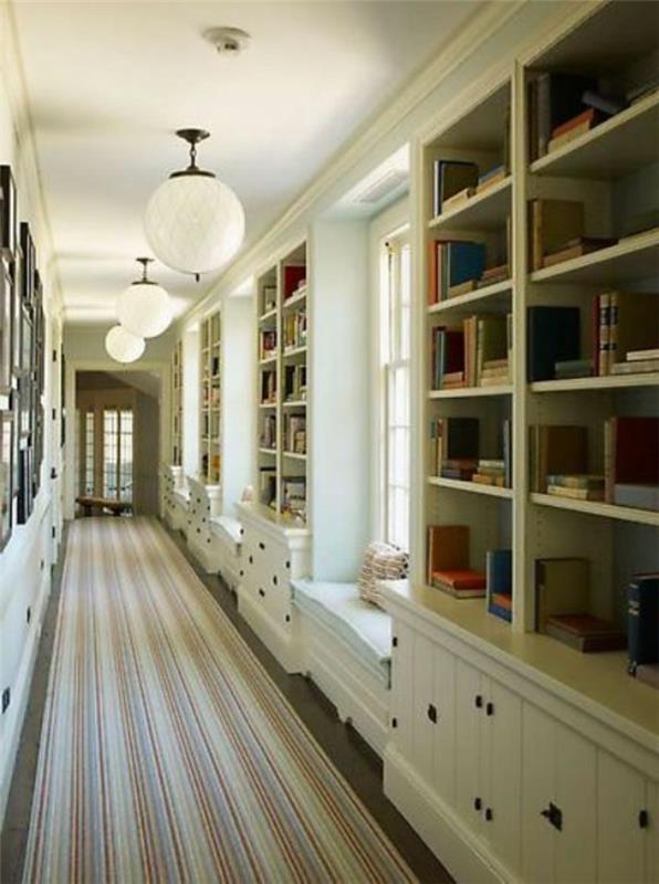 Atviros lentynos su daugybe knygų, ilgas kilimas, siaura prieškambario rūbinė, graži prašmatni įėjimo apdaila