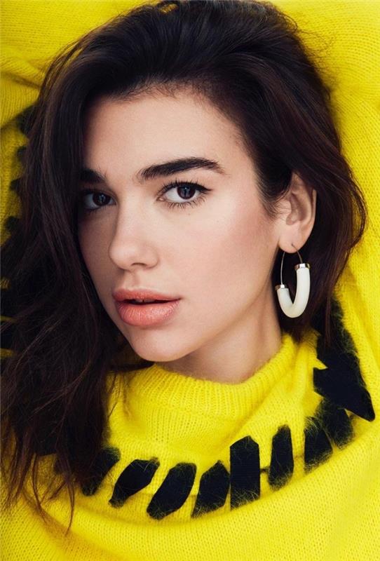 Pričeska Dua Lipa, svetlo rumen model puloverja z okrasno ogrlico v črni barvi, rjavi lasje do ramen