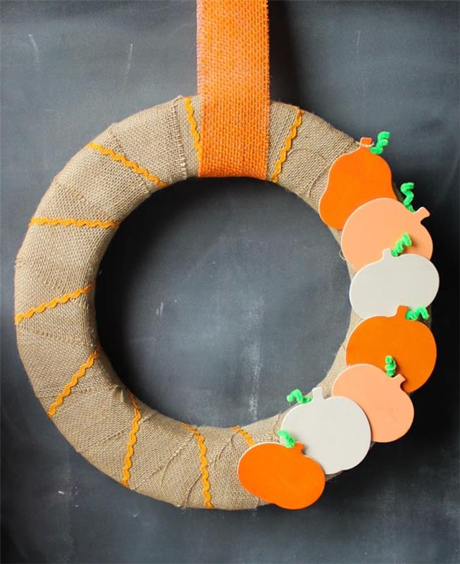 maketa jesenskega venca v mahovem krogu, okrašena s trakom iz jute z deko iz lesenih figuric iz buč z obešanjem na oranžnem traku iz jute