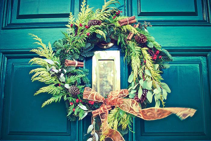 kalėdinis pušų šakų vainikas su pušies pomemomis, holly, cinamonu ir ruda juostele ant smaragdinių žalių durų, kalėdiniai tapetai