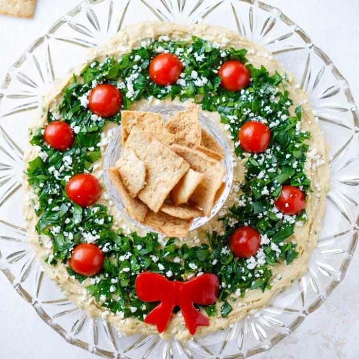 Humus za božični venec s peteršiljem in češnjevim paradižnikom, ki ga skupaj s krekerji postrežejo z originalno božično jedjo, ki jo delite s prijatelji
