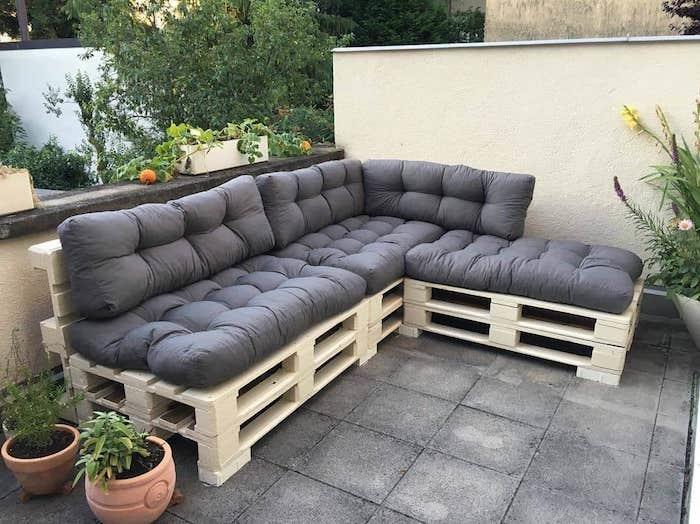 beton plakalar, saksılarla kaplı bir terasta gri koltuk minderli ahşap paletli dolap