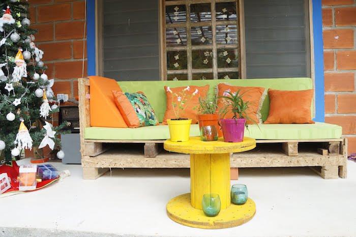 makara masası, fıstık yeşili palet bahçe mobilyası minderi ve turuncu dekoratif minderler, sarı makara ve saksılar
