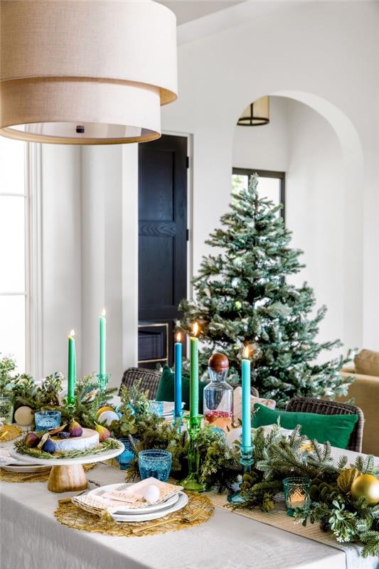 prašmatnaus Kalėdų stalo dekoravimo pavyzdys su žalios ir mėlynos spalvos eglių šakų ir žvakių išdėstymu
