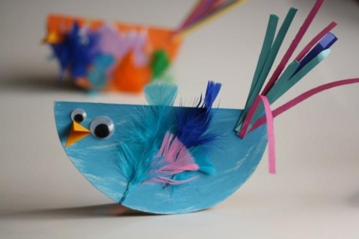 umetniški projekti diy, majhna ročno natisnjena modra ptica, narejena iz papirja, okrašena z modrim in rožnatim perjem, papirnatimi trakovi in ​​očmi
