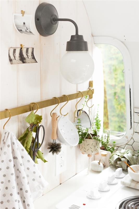 žalvario virtuvės reikmenų laikiklio juosta su mažais kabliukais, sumontuotais ant sienos už viryklės, su senovine sienine lempa, optimizavimo ir mažos virtuvės išdėstymo sprendimais