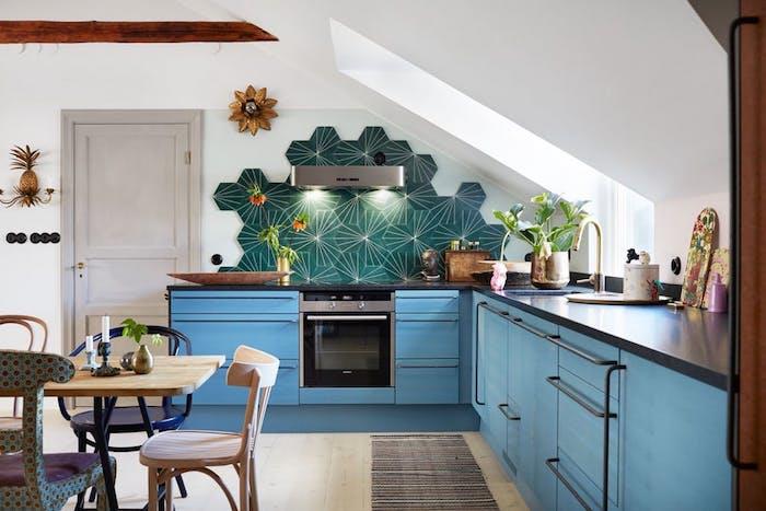 kampinė virtuvė, mėlyni virtuvės baldai, žalios plytelės, pavyzdinė virtuvė po šlaitu, medinis ir metalinis stalas bei senovinės medinės kėdės