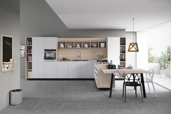 baltas virtuvės modelis su mediniu taškeliu, grindų danga iš akmens plokščių, medinis ir metalinis stalas, balta kėdė ir juoda kėdė, dizainerio pakabinama šviesa