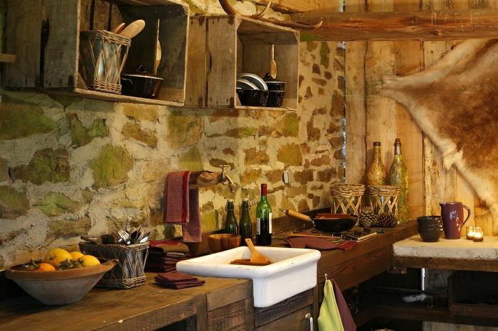 kmečka kuhinja, posoda za sadje, kamnite stene, stenska dekoracija iz umetnega krzna, beli umivalnik, steklenice, omare za palete