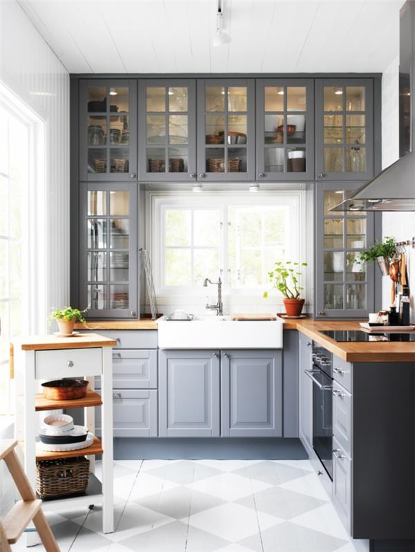 pilka ir balta virtuvė, baltos plytelės, mediniai stalviršiai, pakabinamos stiklo spintelės