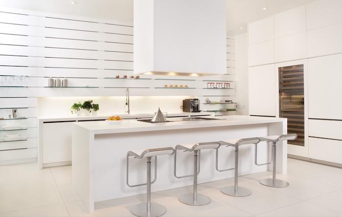 virtuvės pavyzdys su balta centrine sala ir baltais pagrindiniais įtaisais, daugybe atvirų stiklinių lentynų, virtuvės spintelių spintele, nerūdijančio plieno kėdėmis