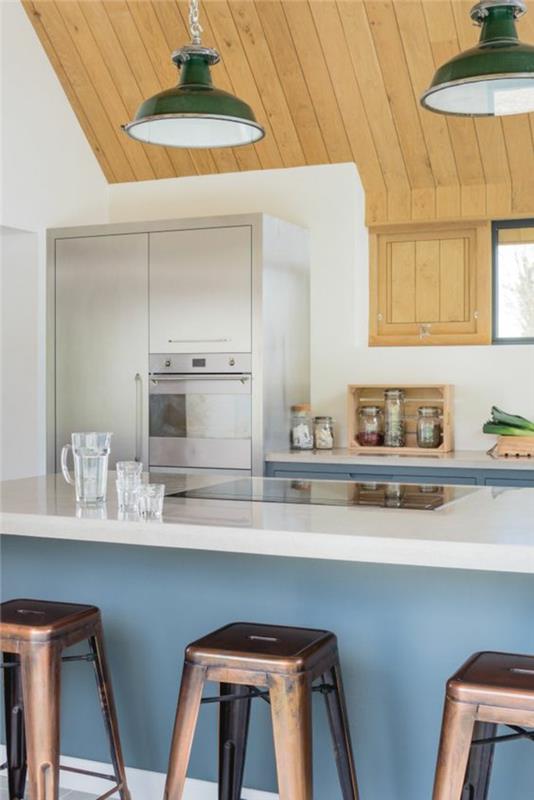 poceni opremljena kuhinja v industrijskem slogu s stropom iz svetlega lesa, zelenimi kovinskimi lučmi in otokom, pobarvanim v pastelno modri barvi z belo delovno ploščo