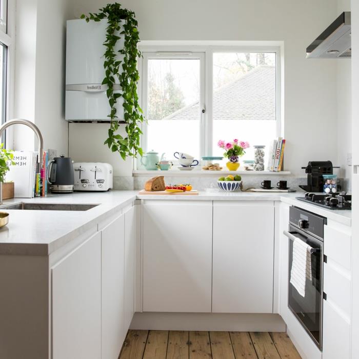 graži balta virtuvė, medinės grindys, baltos spintelės, kvadratinė kriauklė, mažas pakabinamas šaldytuvas, balta lentyna po langu