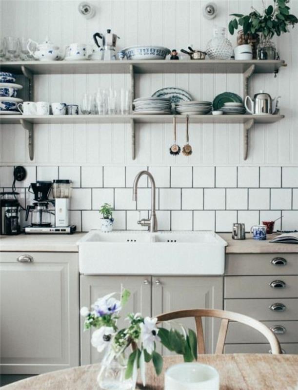 elegantna podeželska kuhinja, bele police, starinsko posodo, siva kuhinjska fasada, bele ploščice, lesena miza in stol