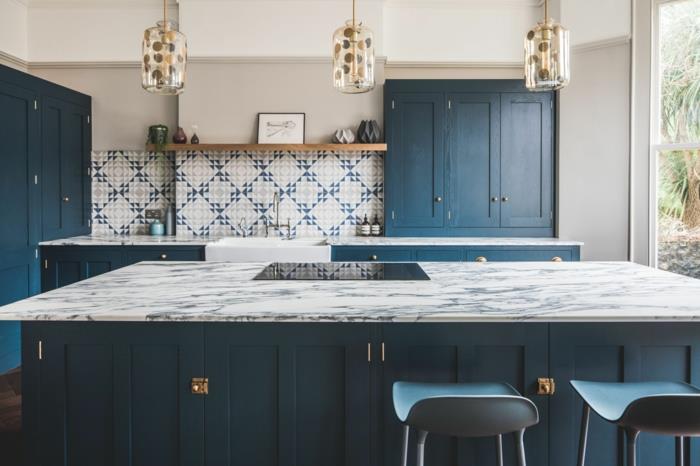 elegantiška virtuvė su sala, baro kėdės, pakabinamos lempos, geometrinės sienų plytelės, mėlynos spintelės