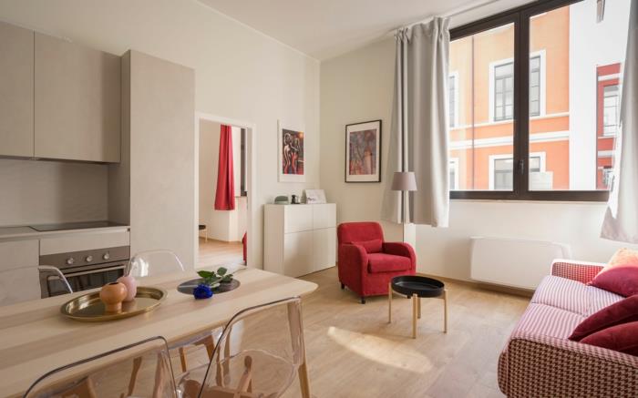 Raudonas fotelis ir balta bei raudona sofa, svetainė ir virtuvė nedidelio buto išplanavime, studentų buto apdaila