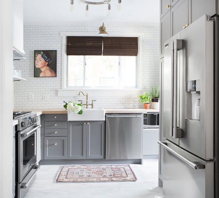 pilka ir balta virtuvė su pilka virtuvės pagrindo spintele ir mediniu stalviršiu, auksinis maišytuvas, baltos sienų plytelės, pilka viryklė, moters portreto sienų apdaila