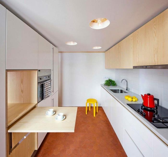dolg prostor, poceni kuhinja, oranžno obarvane ploščice, bela omara z zložljivo mizo iz svetlega lesa, delovna plošča okoli umivalnika v biserno sivi barvi