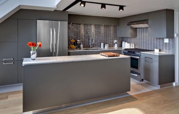 Anglies pilkos spalvos virtuvės išdėstymo idėja su centrine sala ir plaukiojančiomis parketo grindimis