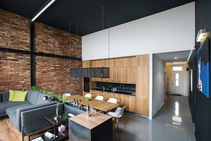 industrijski podstrešni dekor z opečno steno, črno in leseno kuhinjo, odprto za jedilnico z leseno mizo in skandinavskimi stoli, dnevni prostor s sivim kavčem