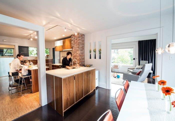 medinė virtuvė su centrine sala, plytų kolona, ​​prožektorių apšvietimas, atsiveriantis į modernų valgomąjį