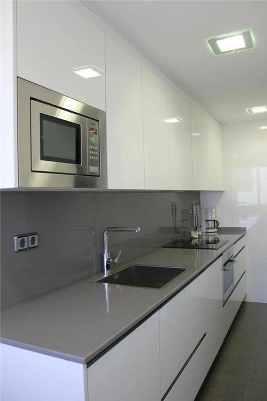 poceni opremljena kuhinja, sijoče sive ploščice, mikrovalovna pečica, vstavljena v belo visečo enoto za shranjevanje, biserno siva delovna plošča, sijajni beli strop s kvadratnimi svetlobnimi reflektorji