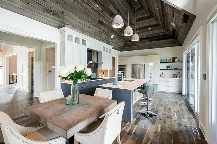 didelė moderni kaimiška virtuvė, medinis valgomojo stalas, didelės patogios kėdės, medinės lentos, sala su kriaukle ir briaunotos virtuvės grindys