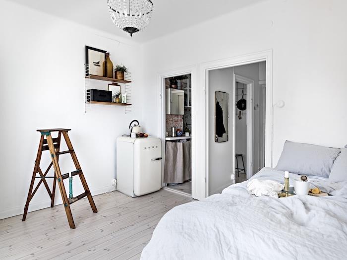 bele stene v sivo -beli spalnici, napol odprti za kuhinjo, lesene in kovinske stenske police, majhna postavitev prostora