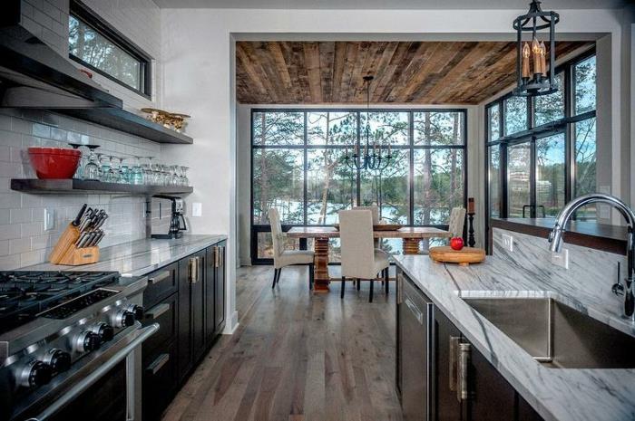 vasarnamio stiliaus virtuvė kontrastingomis spalvomis, juodos spintelės, marmuriniai stalviršiai, kaimiškos išvaizdos medinės lubos, medžio ir marmuro sala
