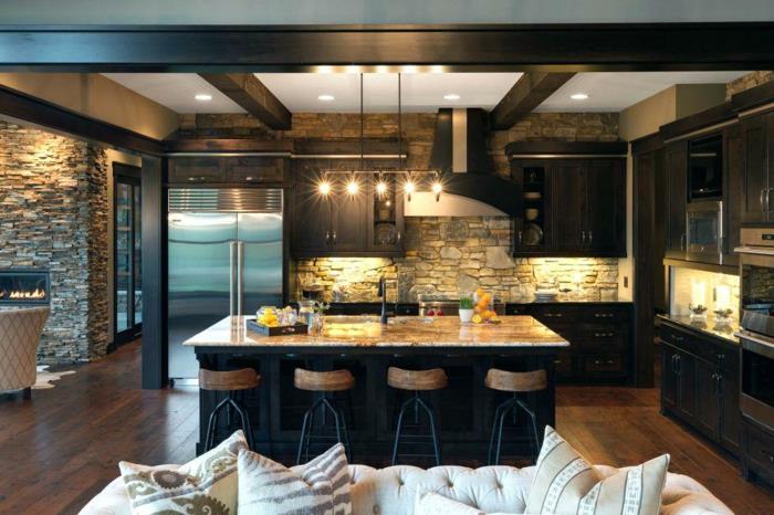 tamsi virtuvė, juoda ir marmurinė sala, medinės ir geležinės baro kėdės, akmens sienų apmušalai, kaimiškos virtuvės grindys