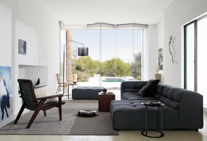 pilka kampinė sofa ir pufas, juoda odinė fotelis, geriausia svetainės sienų spalva, aukštos lubos, pilkas kilimas