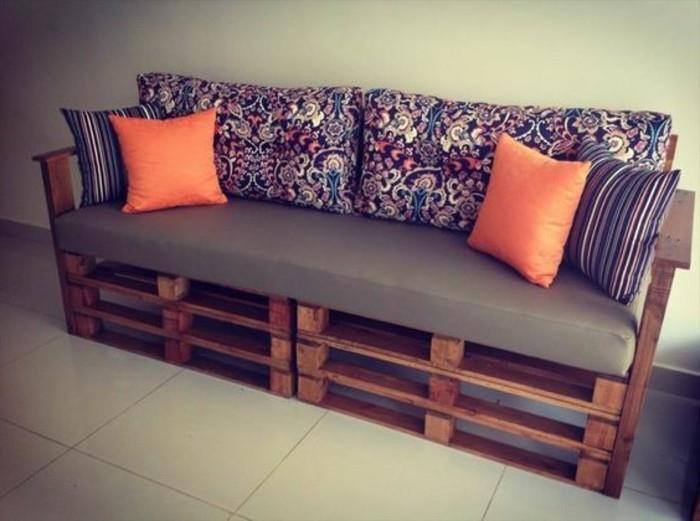 liaudies įkvėptas tamsaus gėlių raštas, ant atlošo pagalvėlių, pasidaryk pats sofa, pagaminta iš tamsiai rudų medinių padėklų, papuošta dviem pagalvėlėmis