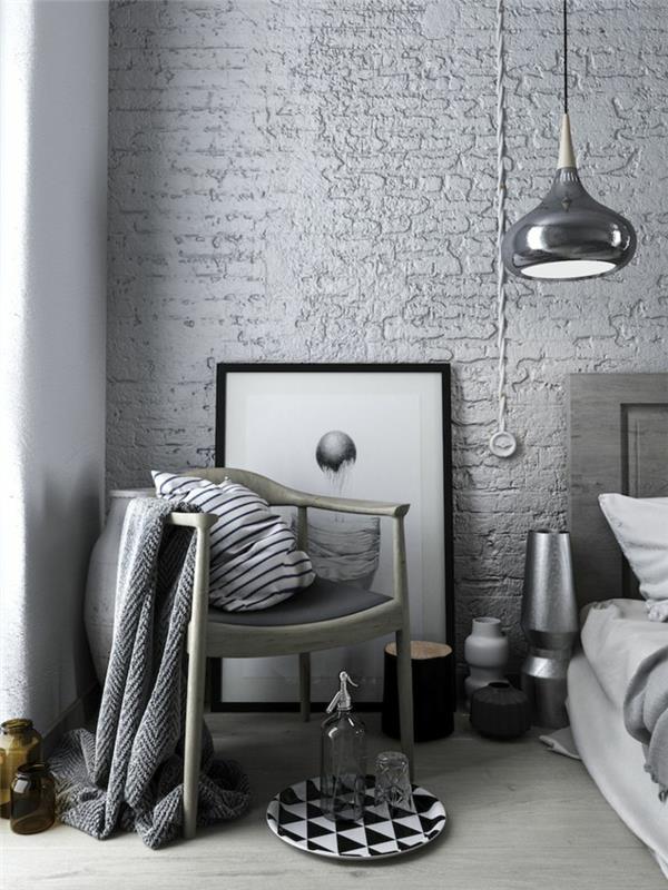 Skandinaviško stiliaus suaugusiųjų miegamojo dekoras, juoda pakabinama lempa, kaimiška kėdė, pledas ir pagalvėlė, lempos ir žvakidės